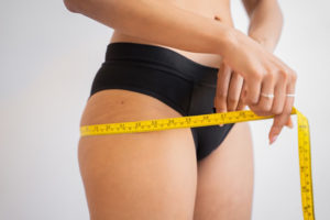 Lady measuring her waist size in black underwear