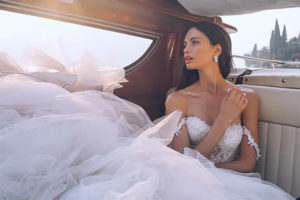 Bride sitting in back of luxurious cars in wedding dress