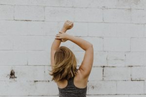 woman with toned arms looking at brick wall confidently
